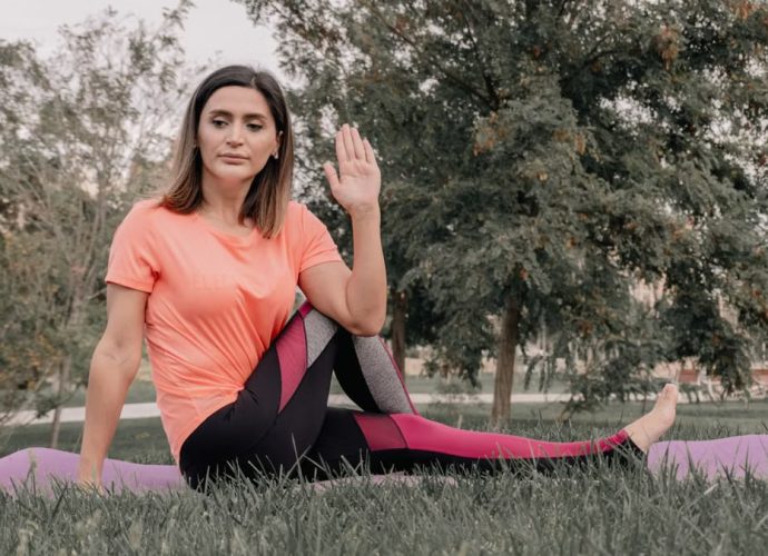 Adult woman practicing yoga on a mat in a park setting, displaying focused concentration.